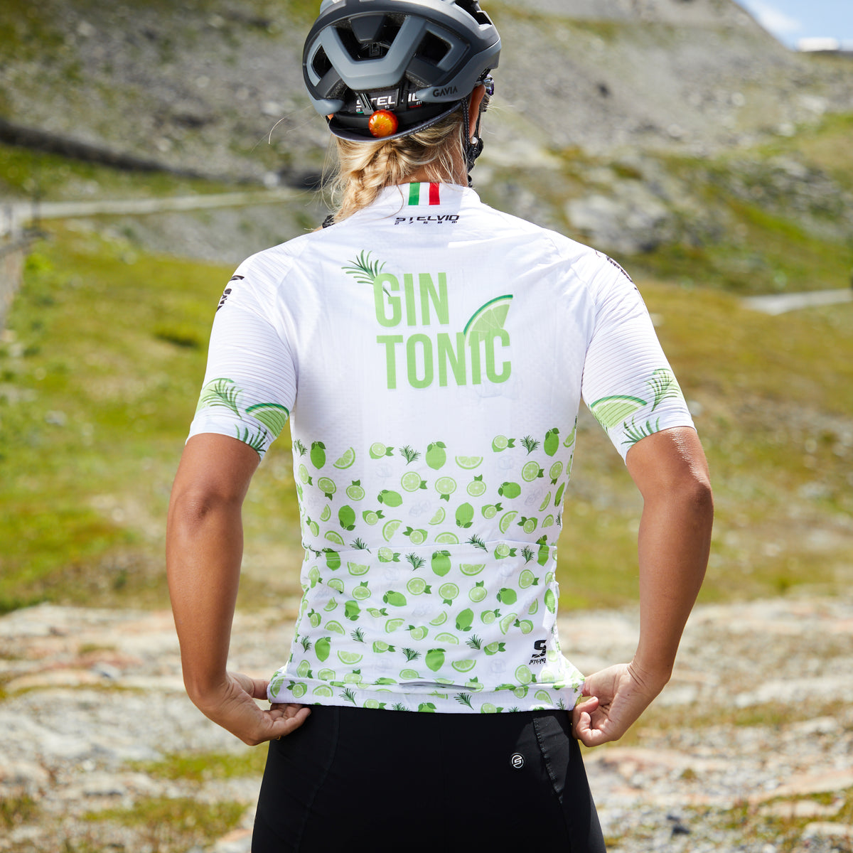 Radfahrerin im Gin Tonic Trikot auf einem Bergpass, Rückansicht